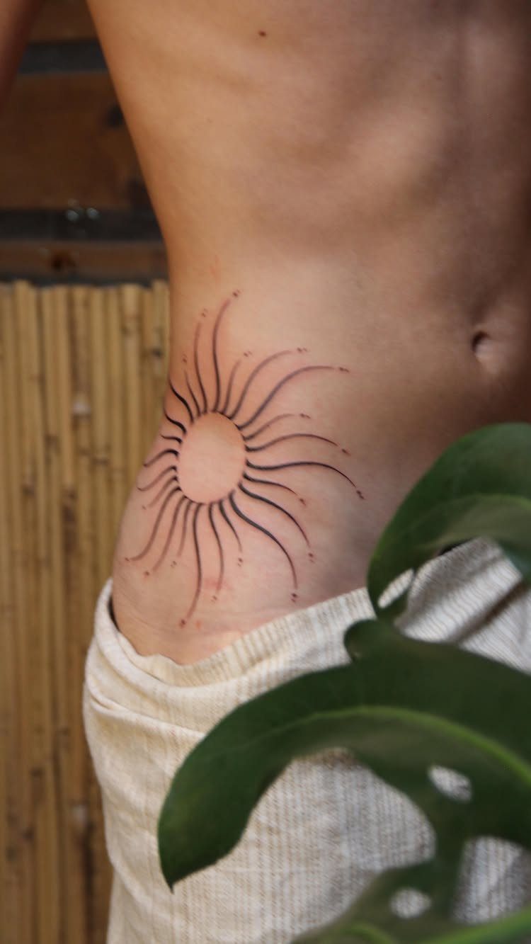 A minimalist sun tattoo with wavy black lines on a person's hip.