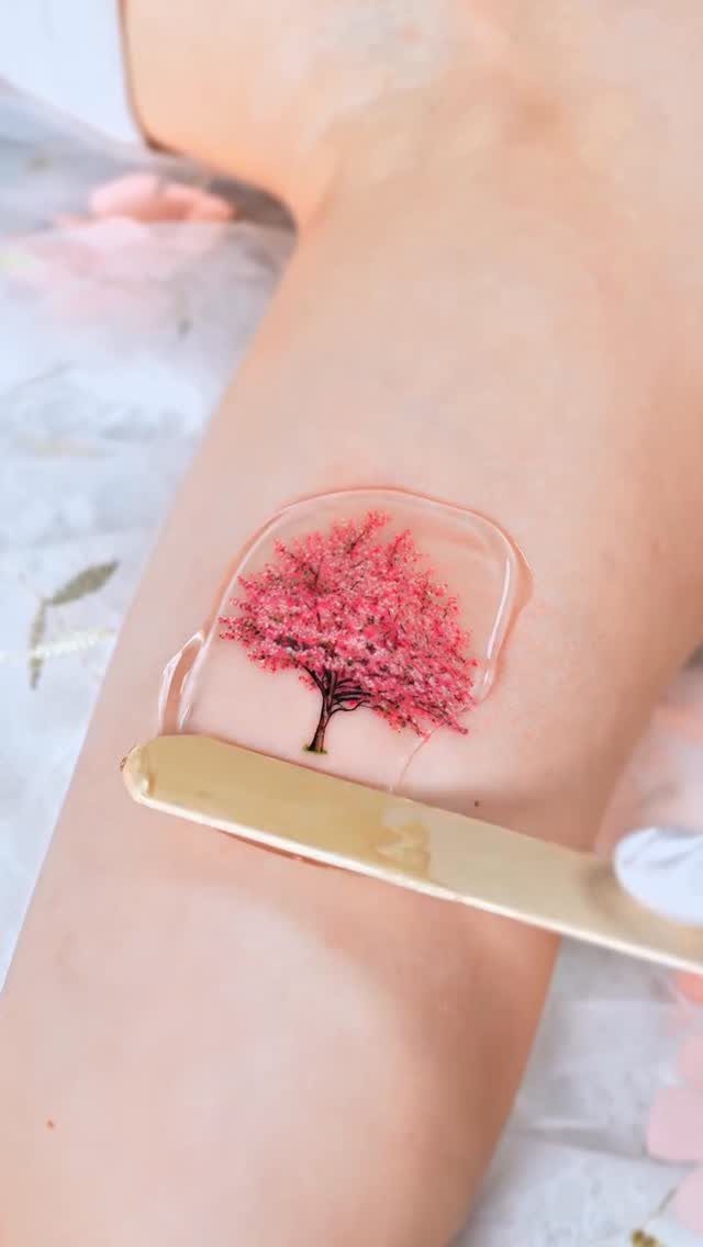 A pink cherry blossom tree tattoo being applied to a person's arm under clear film.