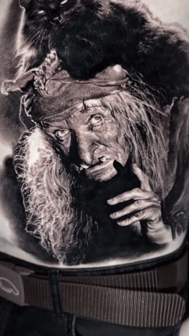 A detailed black and grey realism tattoo of an elderly woman with a dark animal.