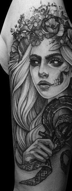 A black and grey tattoo of a woman wearing a floral crown with skull facial markings.