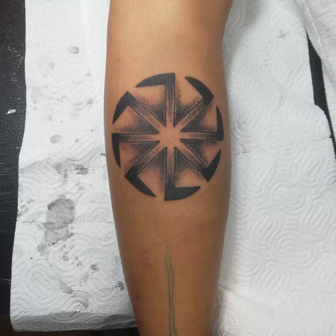 A black ink geometric sun wheel tattoo on a person's forearm.