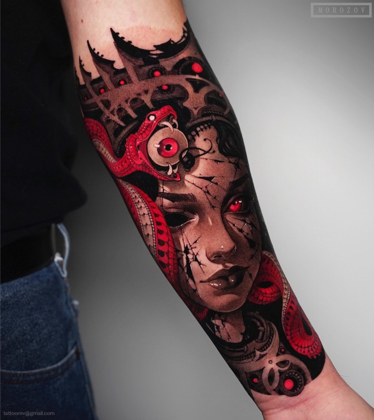 A detailed black and red tattoo of a woman's face with a snake on a forearm.