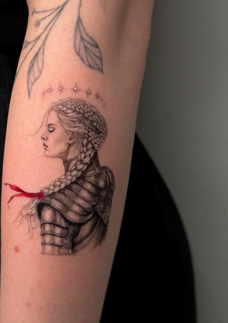 A detailed black and grey tattoo of a woman with braided hair and stars on an arm.