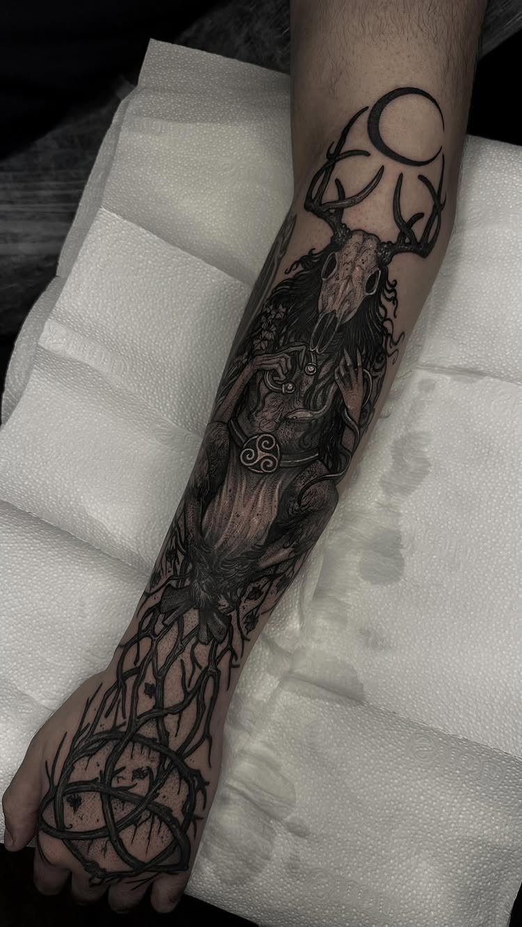 A detailed black ink forearm tattoo featuring a deer skull, antlers, and crescent moon.