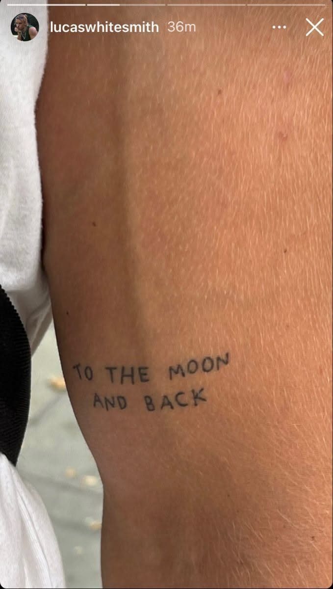 A small black ink tattoo on a person's leg reading TO THE MOON AND BACK.