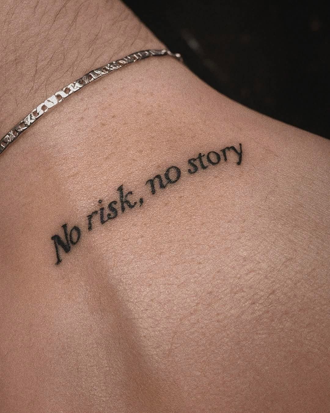 A small black cursive tattoo reading No risk, no story on a person's collarbone.