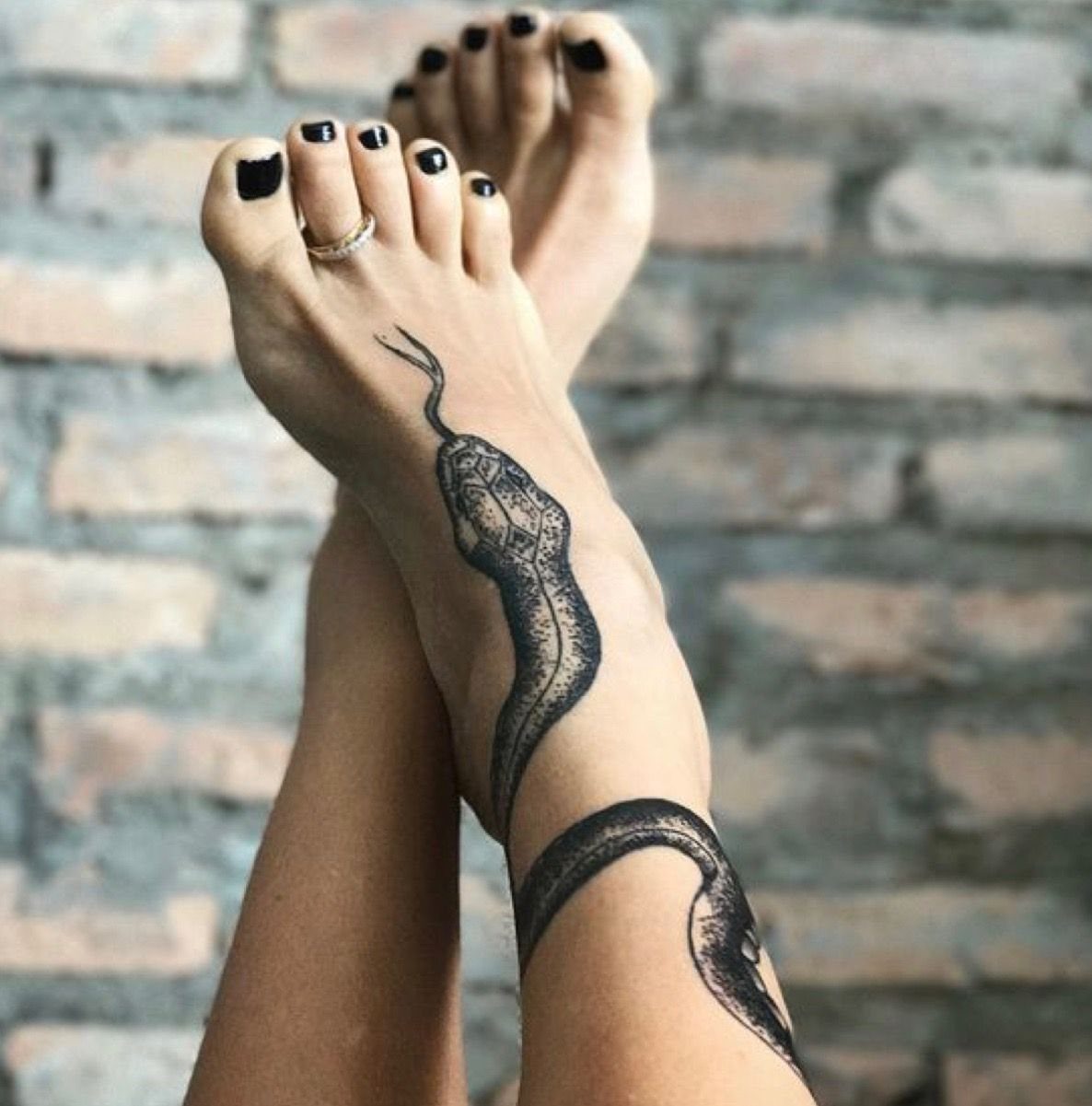 A black ink snake tattoo winding around a person's ankle and across the top of their foot.