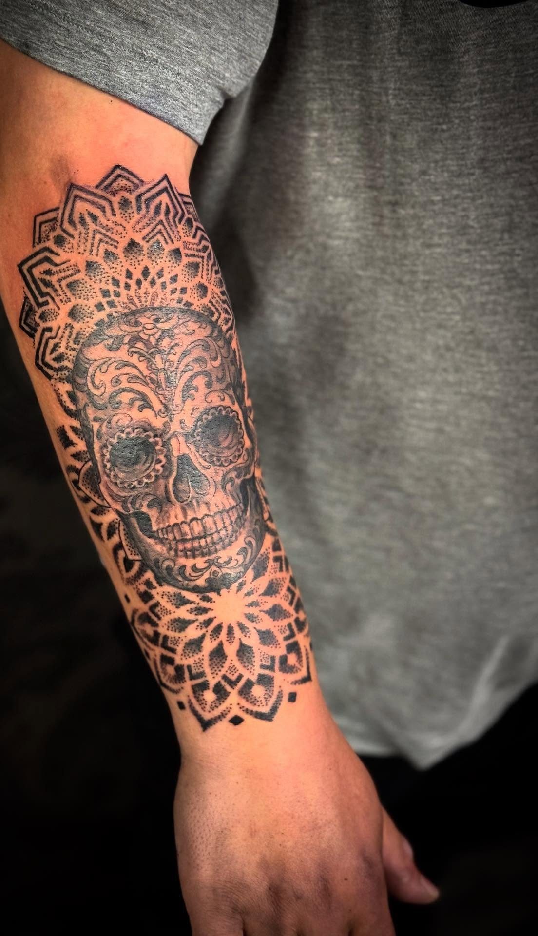 A black and grey sugar skull tattoo with intricate geometric mandala patterns on a forearm.