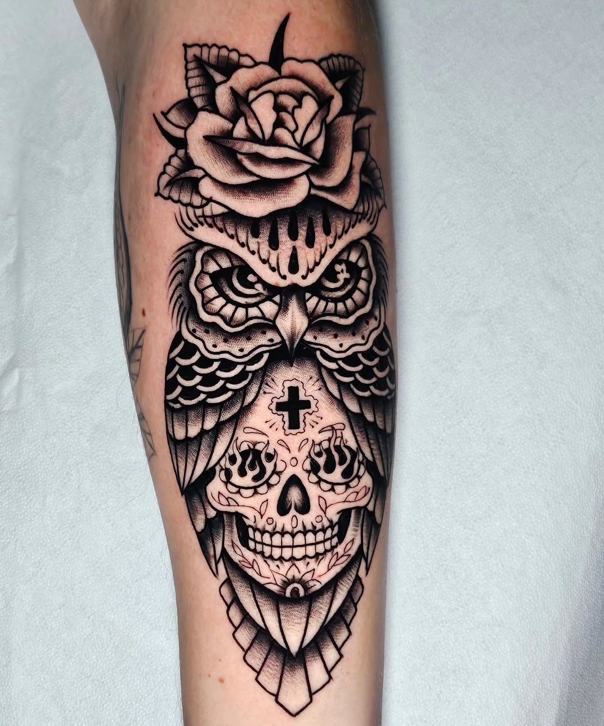 Black and grey tattoo of an owl with a sugar skull face and a rose on an arm.