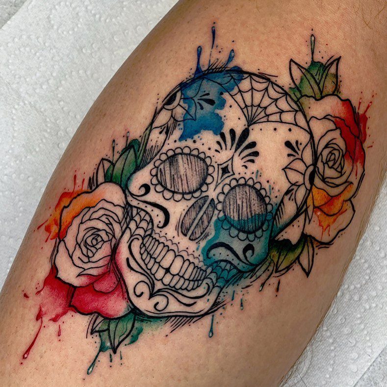 A sugar skull tattoo with colorful watercolor splashes and roses on human skin.