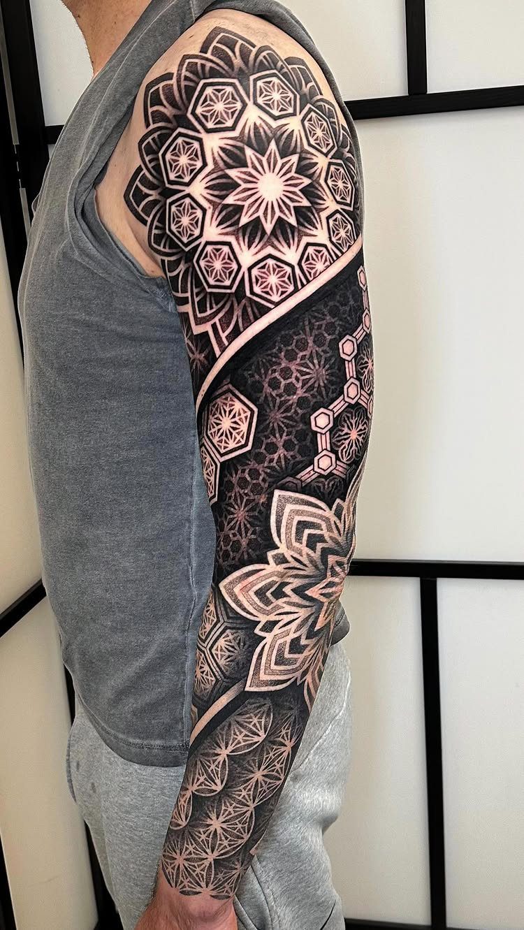 A man's arm displaying an intricate black ink mandala and geometric pattern sleeve tattoo.