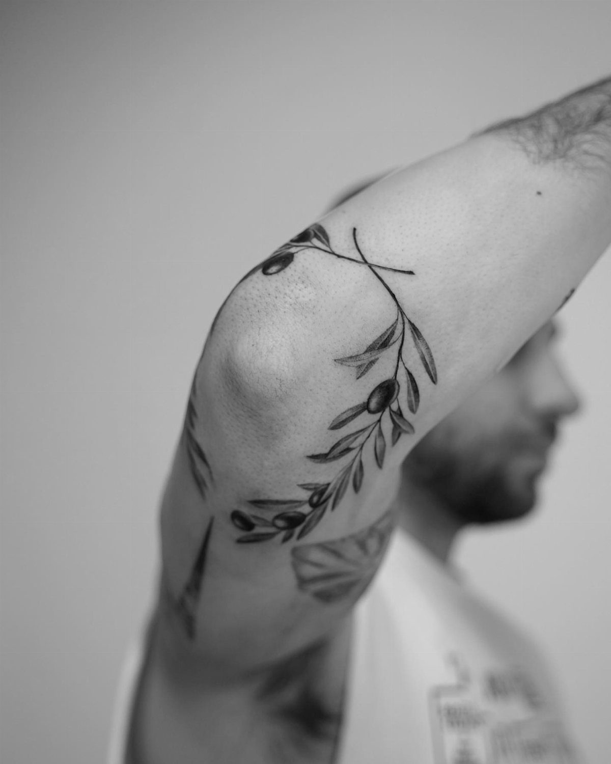 A black and white tattoo of olive branches with leaves and olives on a man's arm.