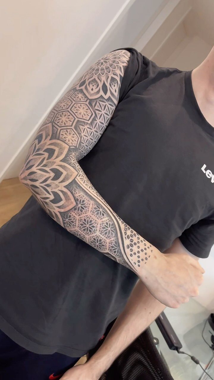 A man's arm covered in a detailed black ink geometric and mandala sleeve tattoo.