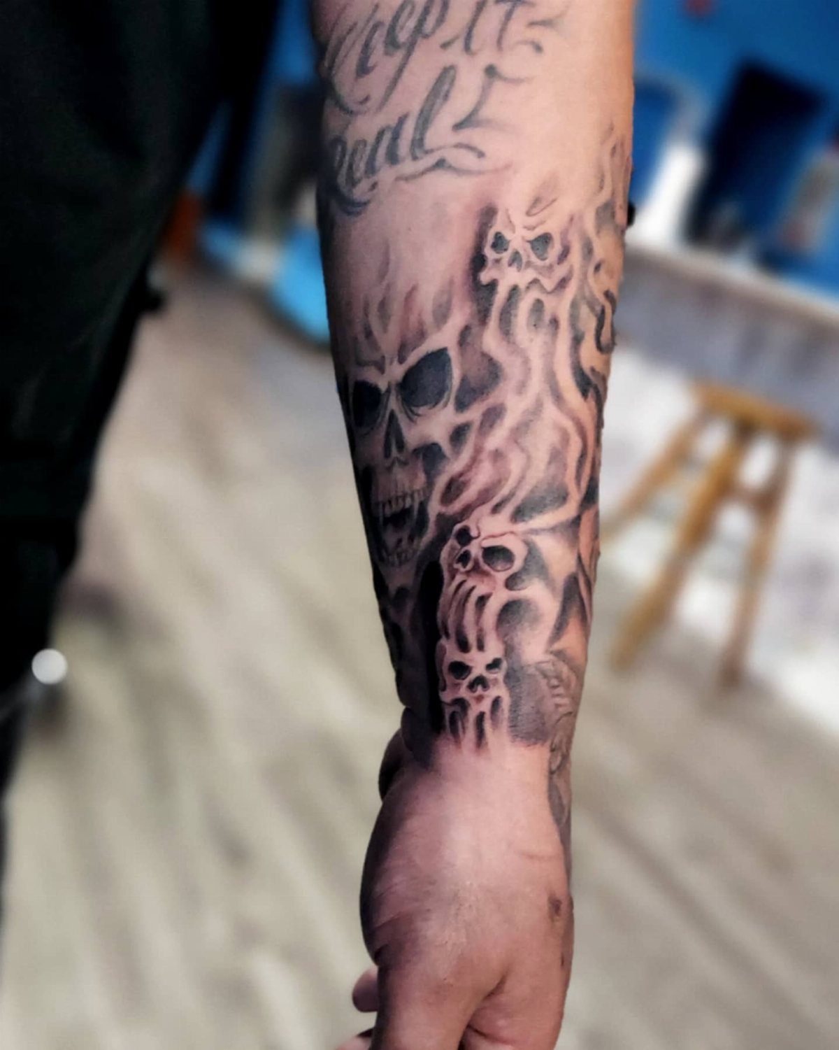 A forearm tattoo featuring several skulls intertwined with flowing, dark smoke-like patterns.