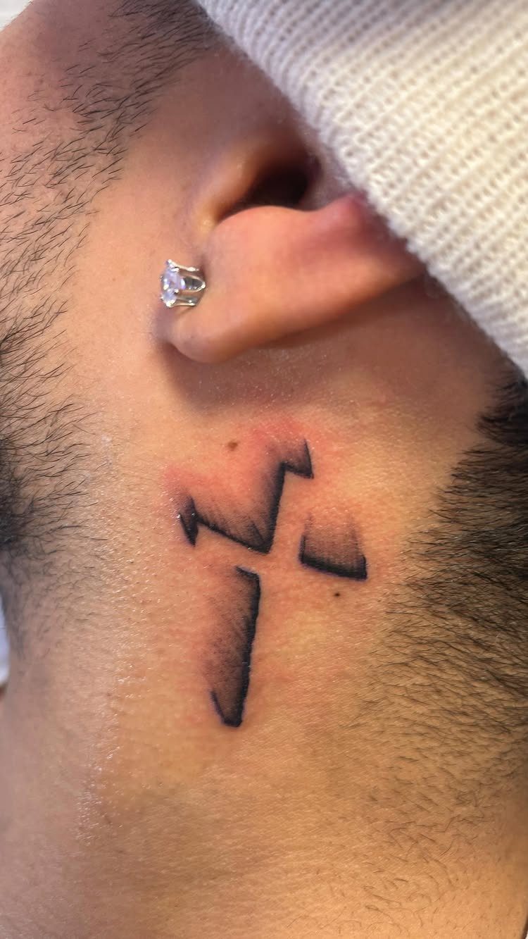 A small black ink 3D shaded cross tattoo on a person's neck.