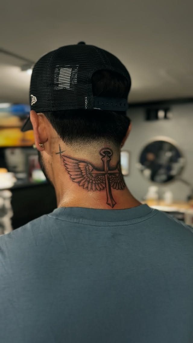 A man with a tattoo of a cross with angel wings on his neck.
