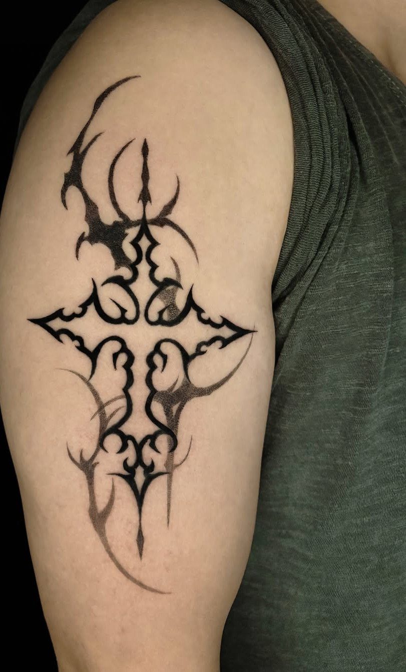 A black tribal style tattoo of a stylized cross on a person's arm.