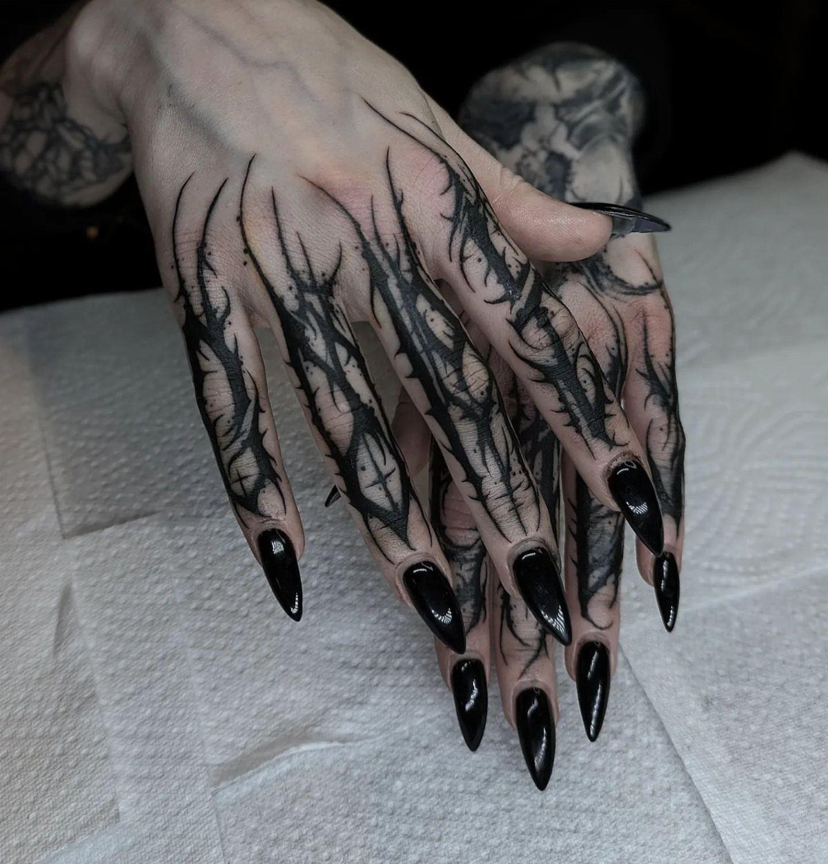 8 Tattoo Pattern Gothic Ideas: From Crows to Cathedral Arches 4 Hands with long black nails featuring intricate smoky black gothic line tattoos.