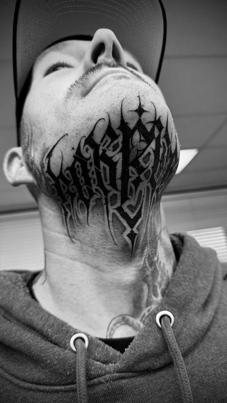8 Tattoo Pattern Gothic Ideas: From Crows to Cathedral Arches 5 A man with a large black gothic lettering tattoo on his chin and neck.
