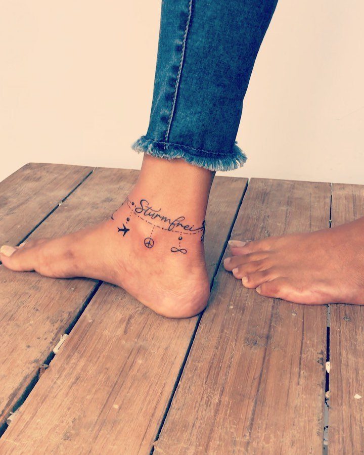 16 Word Tattoo Placement Ideas: From Spine to Finger 12 A person's ankle featuring a delicate word and symbol tattoo resting on wooden planks.
