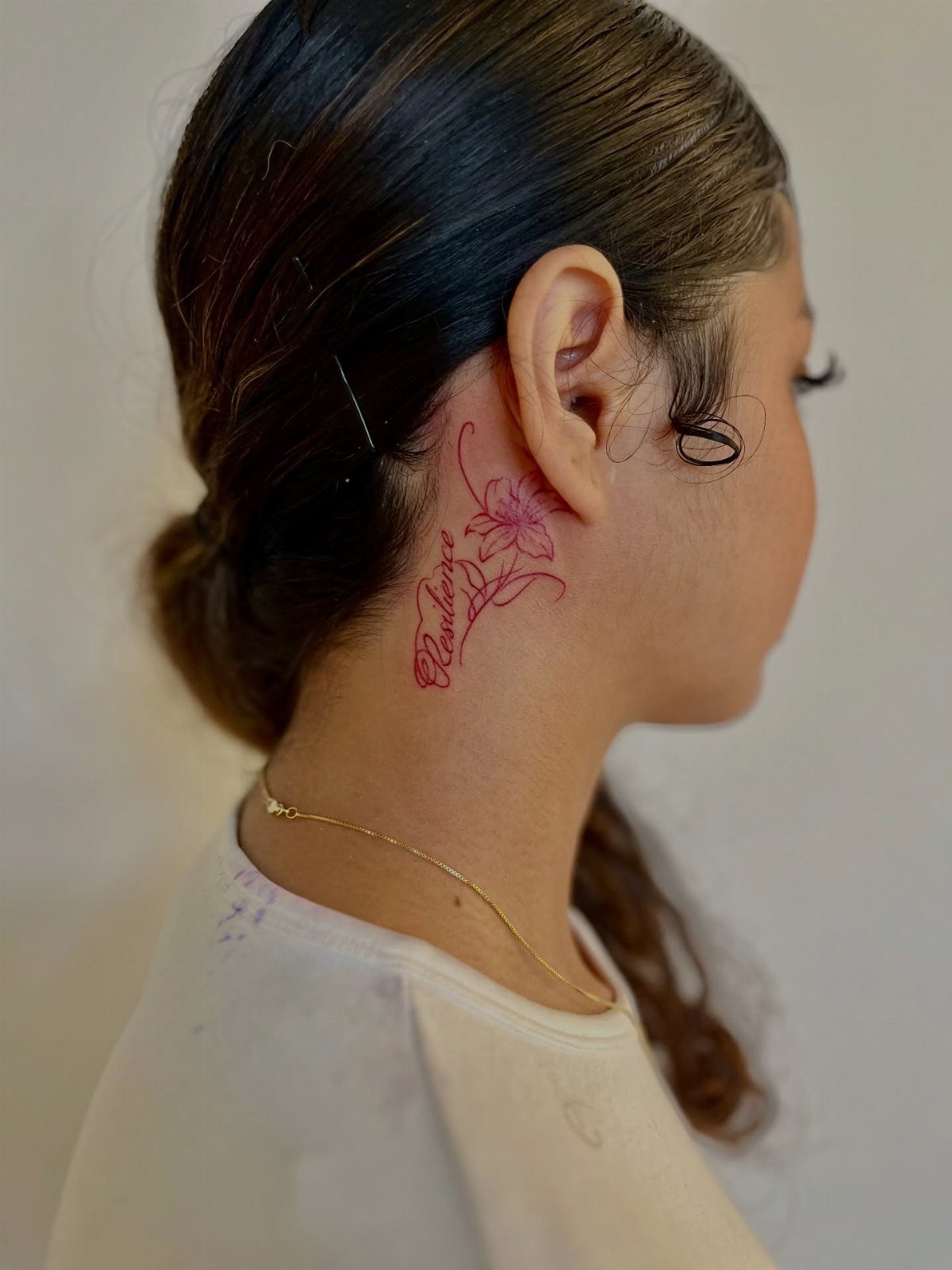 16 Word Tattoo Placement Ideas: From Spine to Finger 10 A person's profile showing a red floral and script tattoo behind the ear and on the neck.