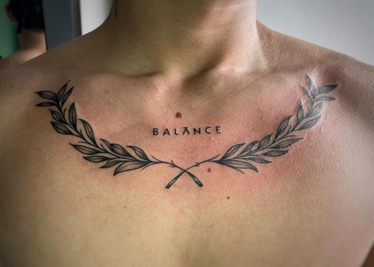 16 Word Tattoo Placement Ideas: From Spine to Finger 7 A black ink tattoo of the word BALANCE between two laurel branches on a person's chest.
