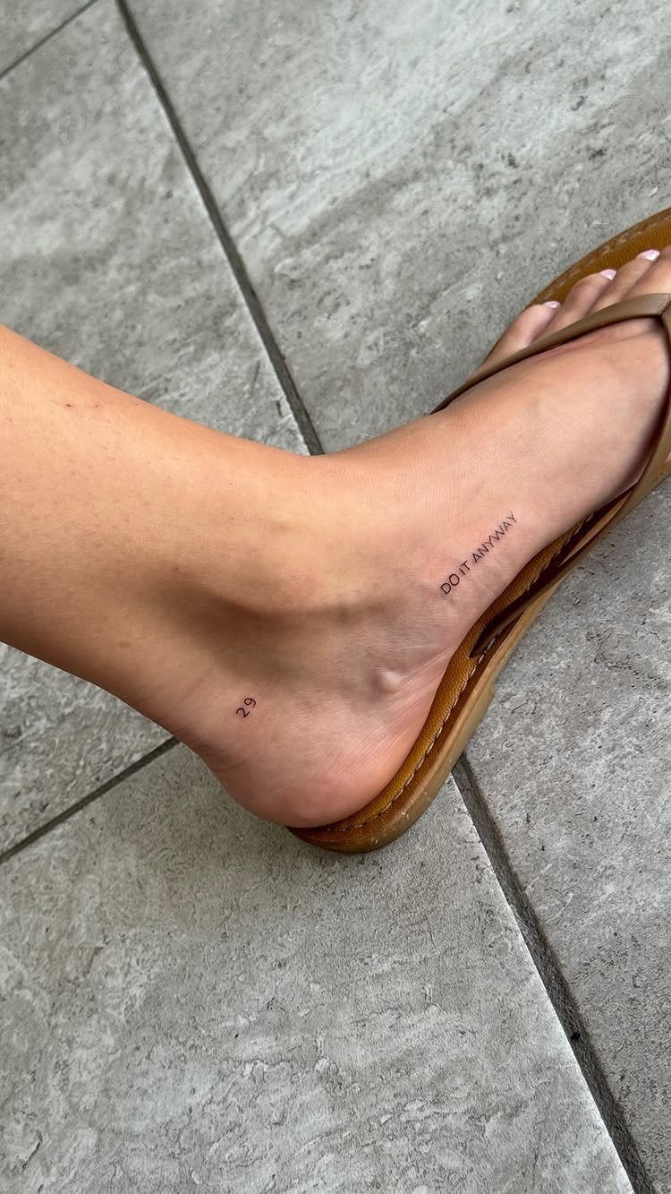 16 Word Tattoo Placement Ideas: From Spine to Finger 14 A person's foot with small word tattoos wearing a brown flip-flop on grey tiles.