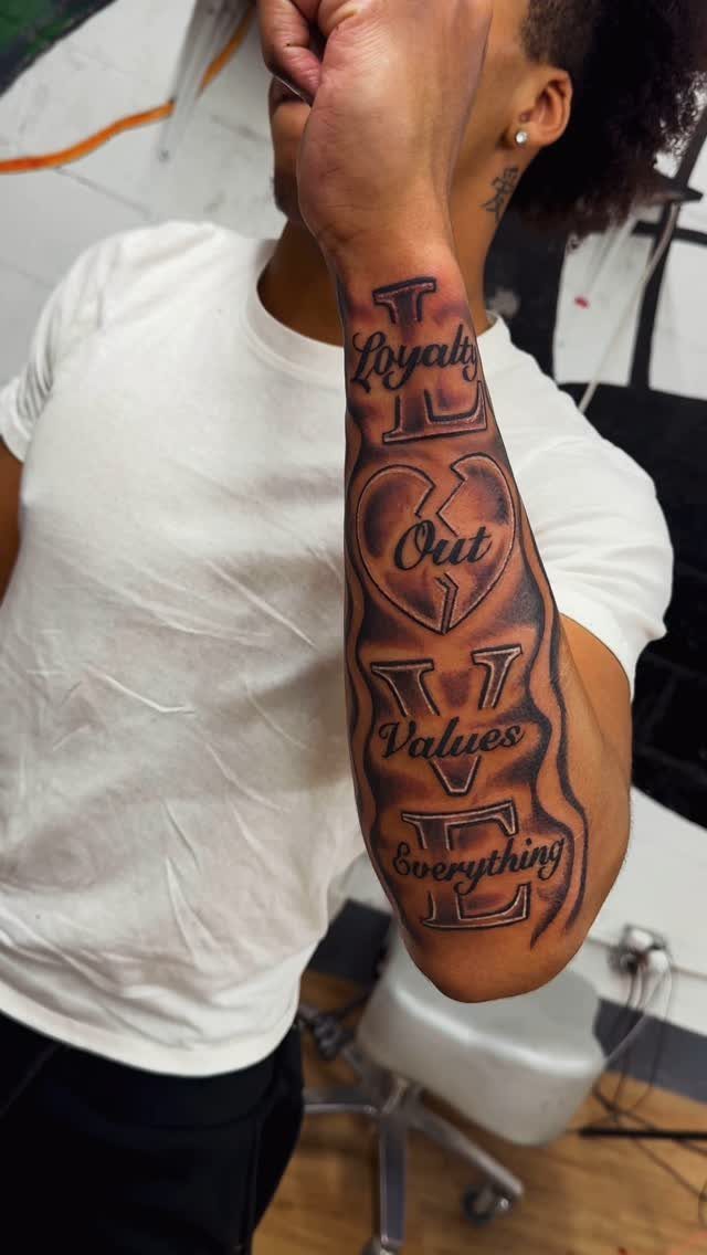 16 Word Tattoo Placement Ideas: From Spine to Finger 1 A person's forearm displaying a large black and grey tattoo with the words Loyalty Out Values Everything.