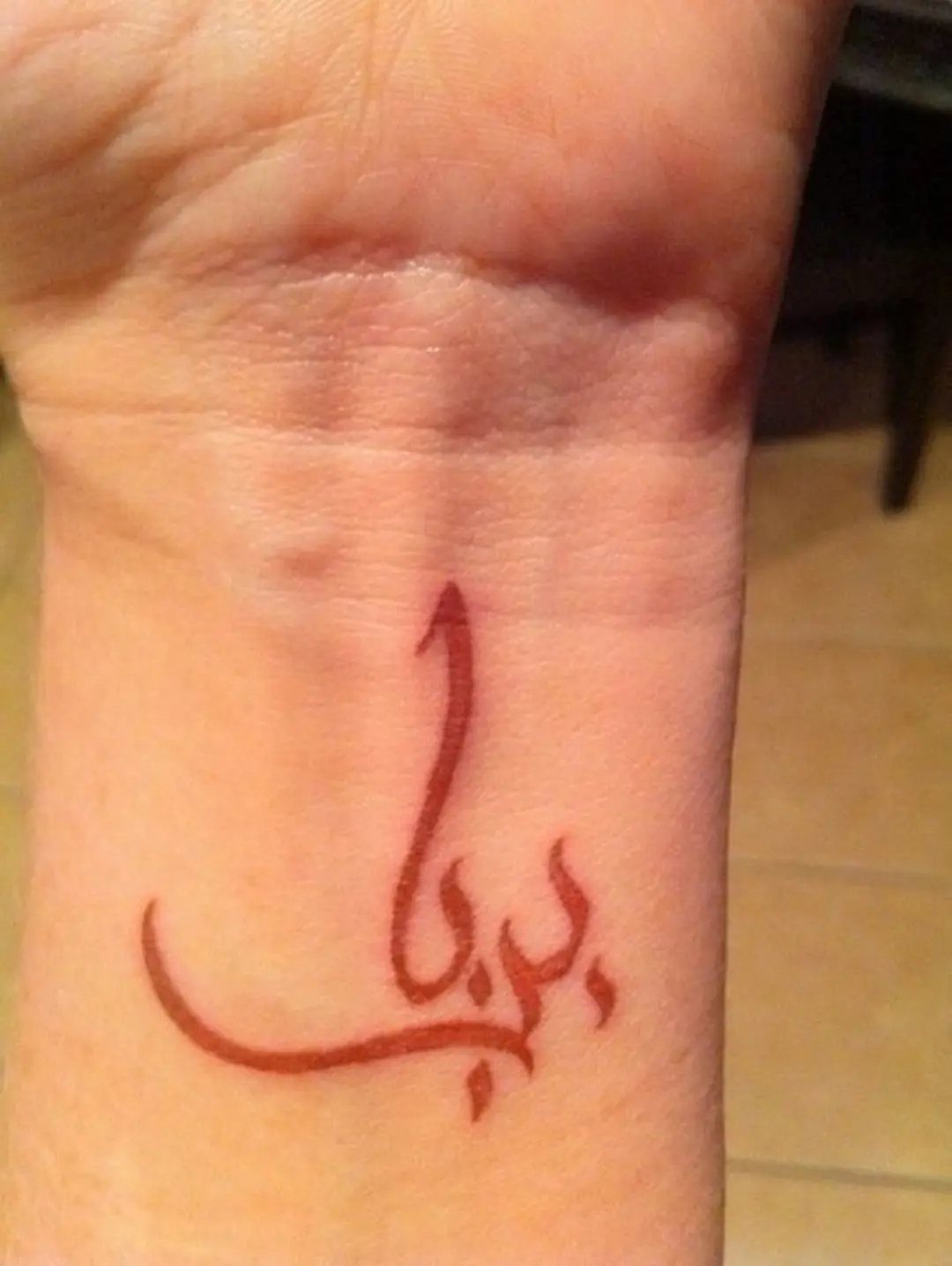 16 Word Tattoo Placement Ideas: From Spine to Finger 2 A red ink Arabic calligraphy tattoo on a person's inner wrist.