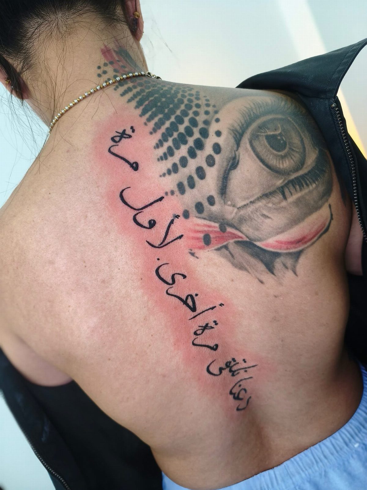 16 Word Tattoo Placement Ideas: From Spine to Finger 4 A large tattoo of a realistic eye and vertical Arabic script on a person's upper back.