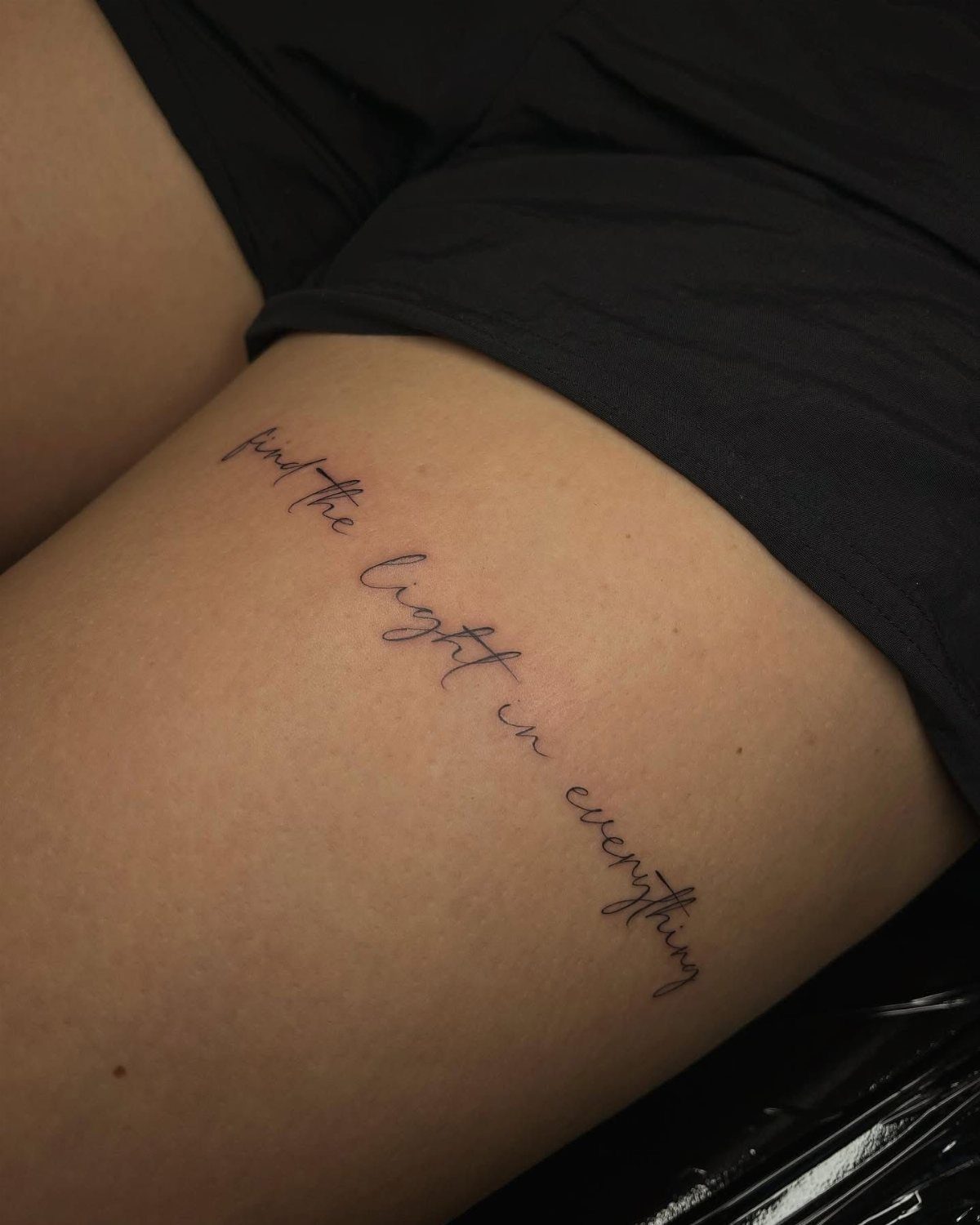16 Word Tattoo Placement Ideas: From Spine to Finger 11 Cursive script tattoo reading 'find the light in everything' on a person's thigh.