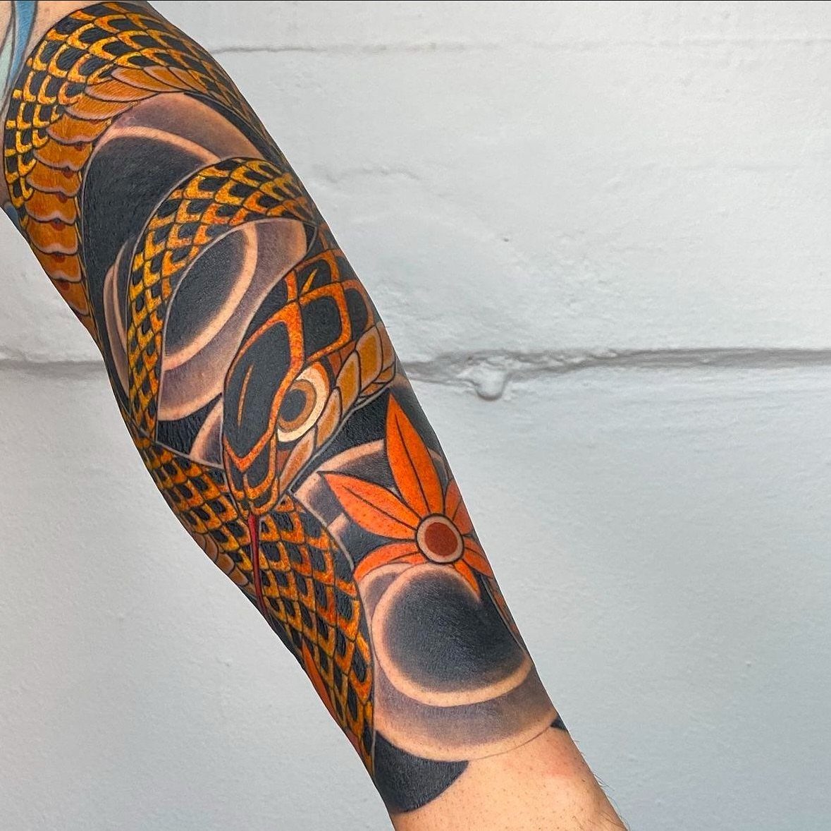 A detailed Japanese style tattoo with orange scales and maple leaf on a person's forearm.