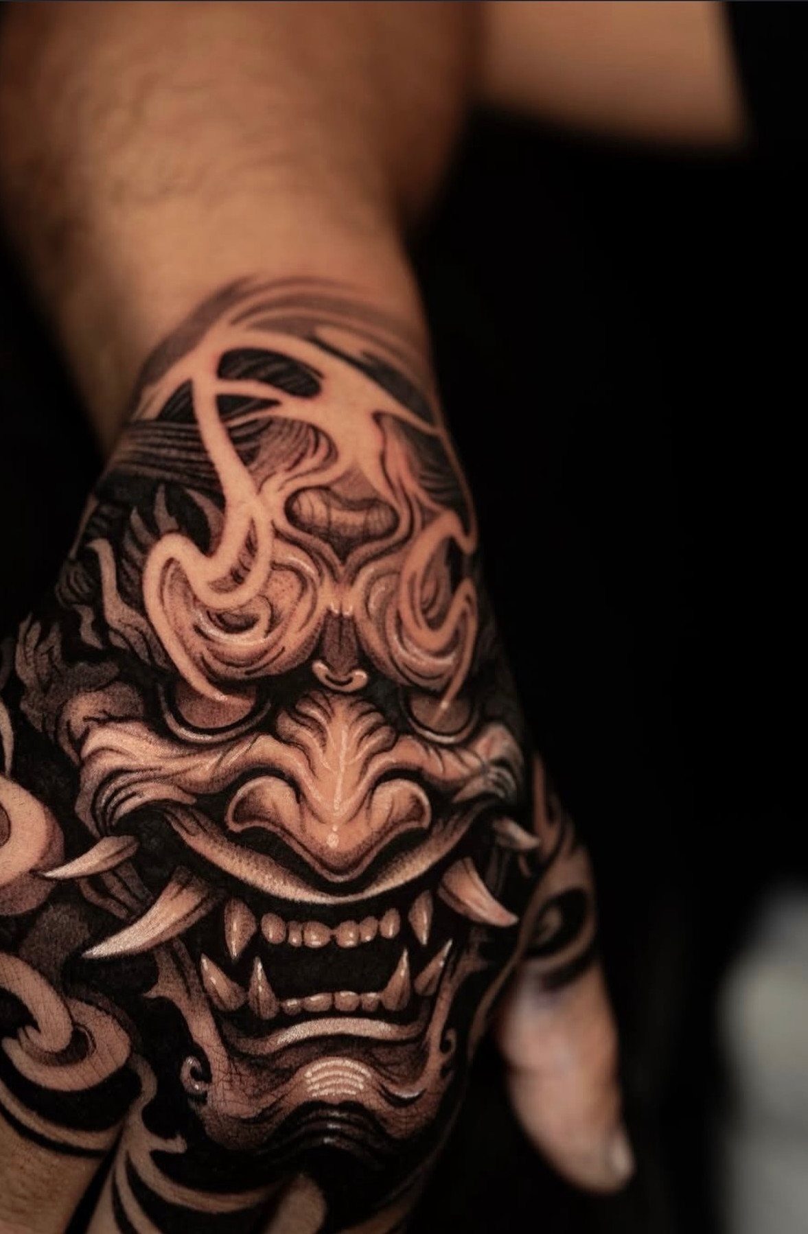 A detailed black and grey Hannya mask tattoo covering a person's hand and knuckles.