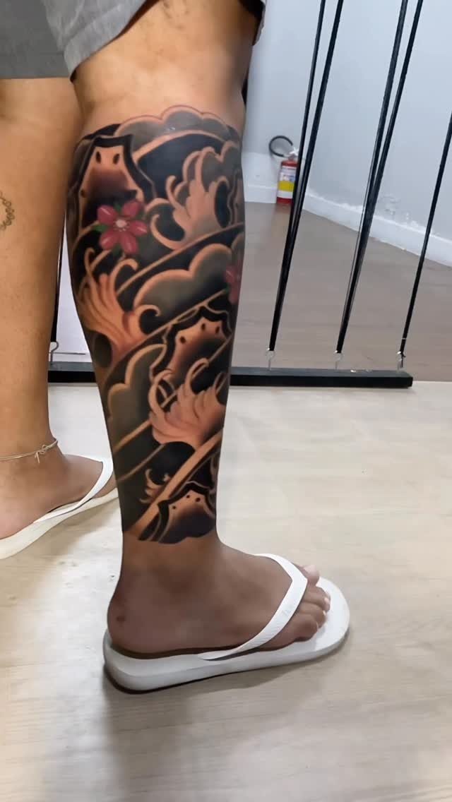 A large Japanese style leg tattoo featuring waves and red flowers on a person's calf.