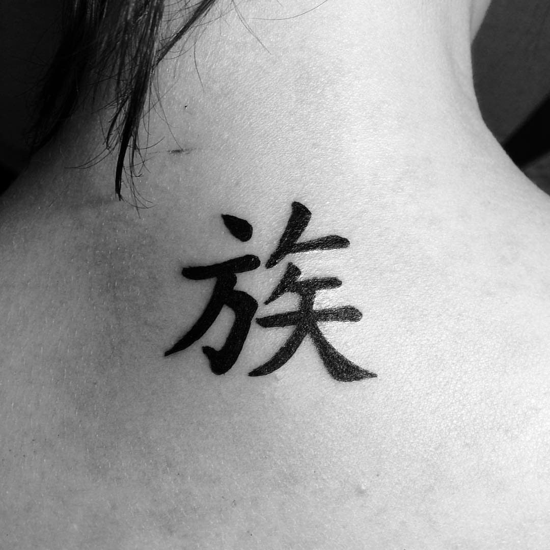 A black ink kanji tattoo centered on the upper back and nape of a person's neck.