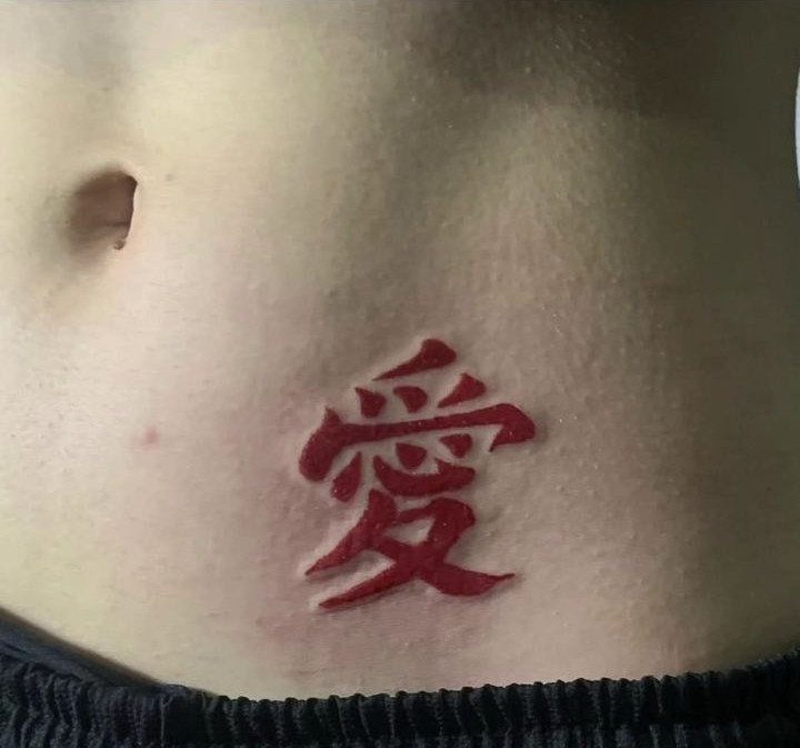 A red kanji tattoo on a person's lower abdomen near the hip area.