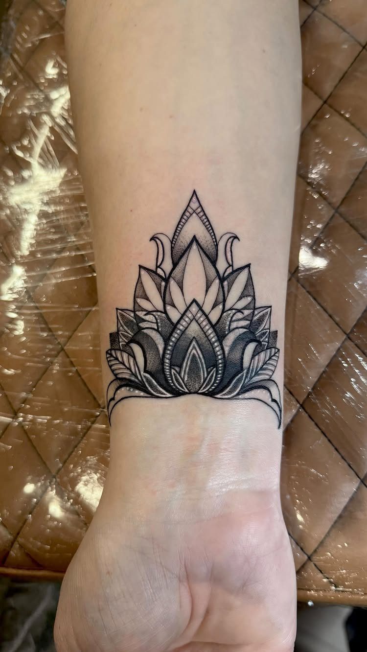 A black ink lotus flower tattoo centered on a person's inner wrist.