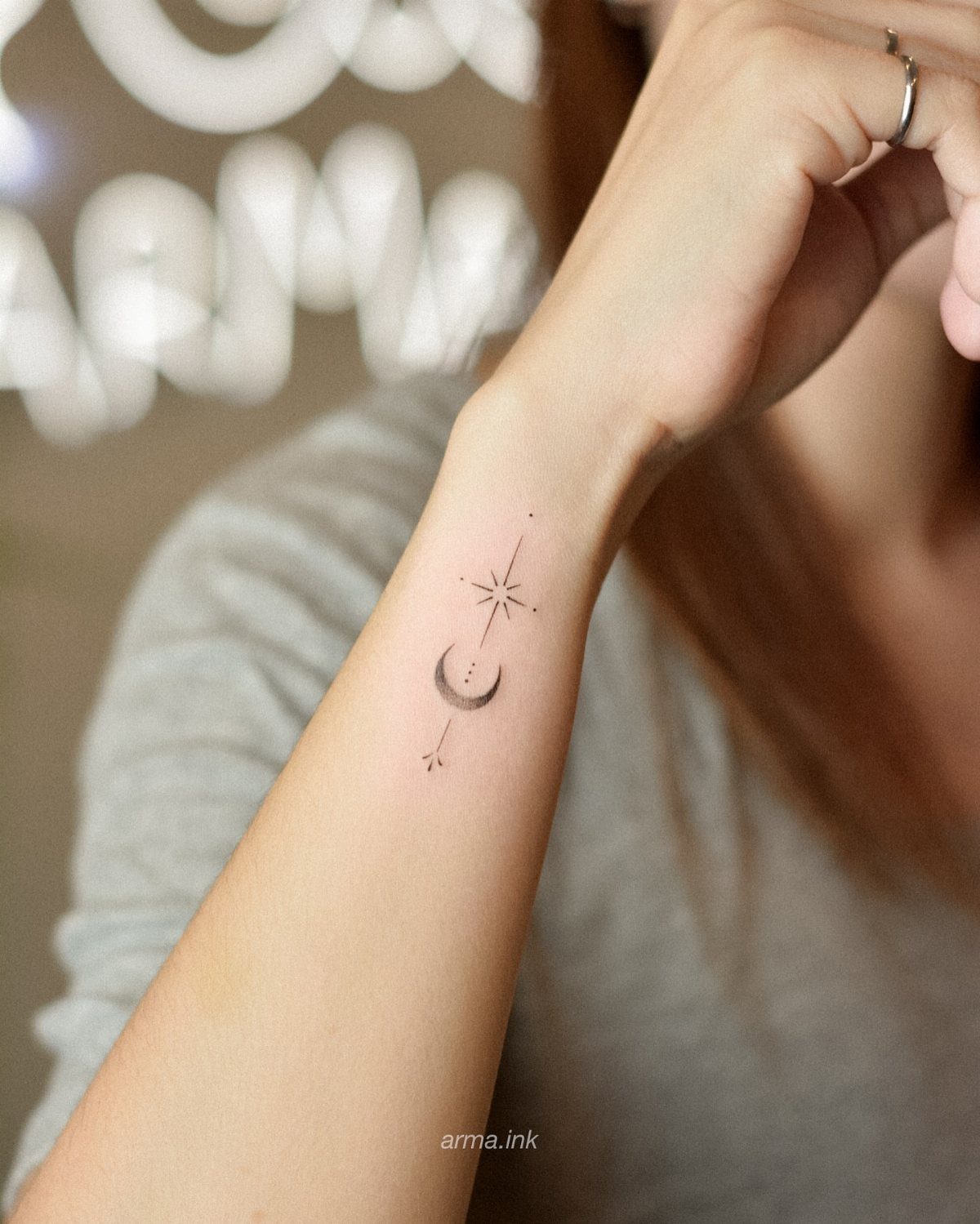 A minimalist crescent moon and star tattoo on the side of a person's wrist.