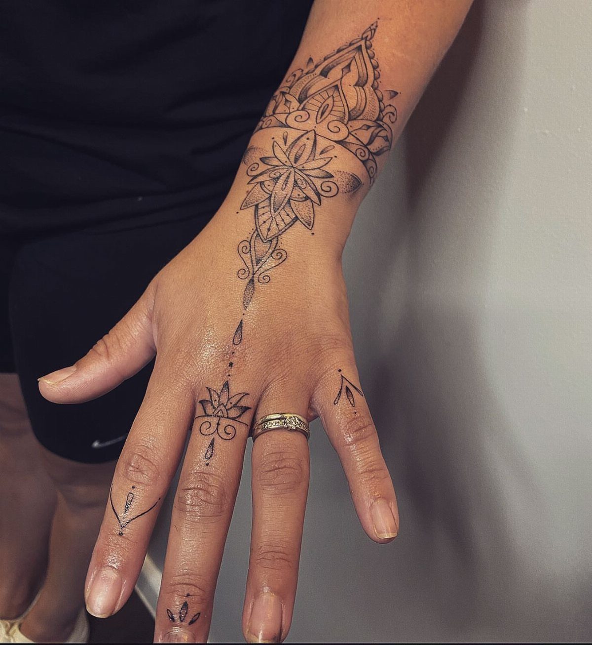 A hand and wrist decorated with intricate black ink floral and mandala style tattoos.