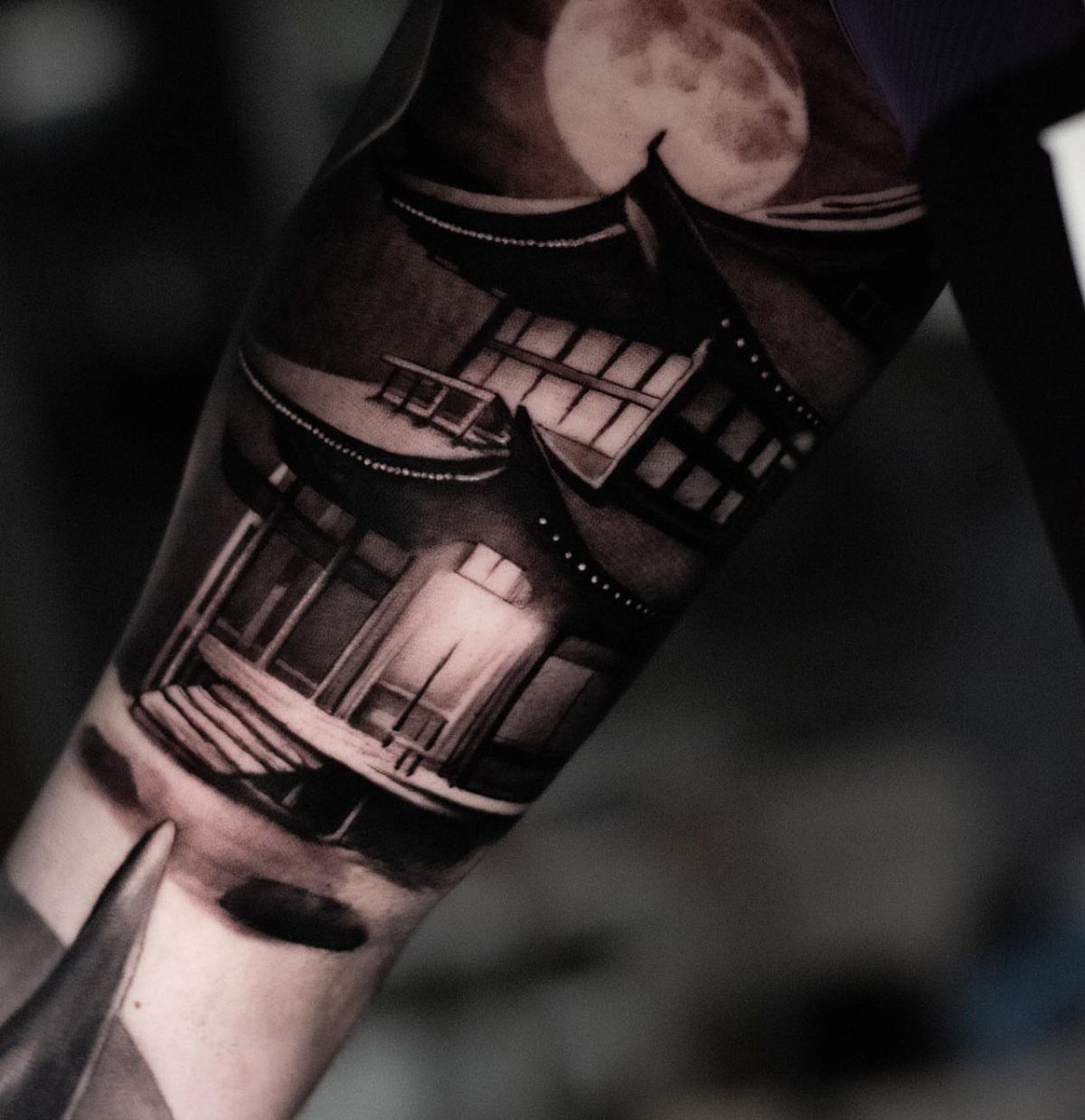 7 Tattoo Style Home Designs for Your Next Ink 3 A black and grey tattoo of a traditional Japanese house under a large moon on an arm.