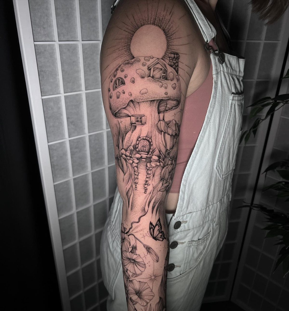 7 Tattoo Style Home Designs for Your Next Ink 5 A detailed black and grey tattoo of a mushroom house on a person's upper arm.