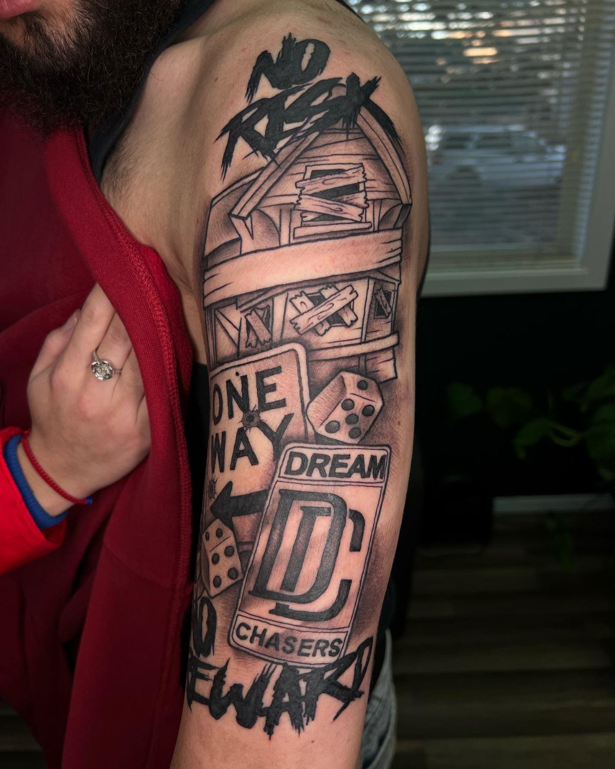 7 Tattoo Style Home Designs for Your Next Ink 4 A black and grey tattoo on an arm featuring a boarded-up house and dice.