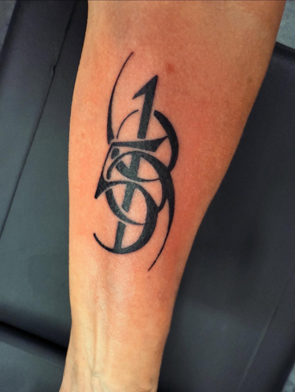 A black ink tattoo of ornate, stylized numbers on a person's forearm.