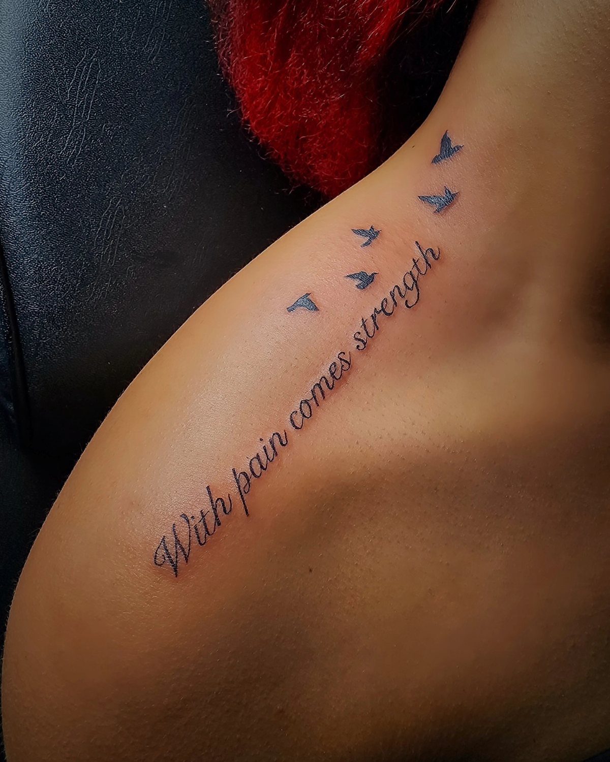 Fine line script tattoo on a person's shoulder with small bird silhouettes flying above the text.