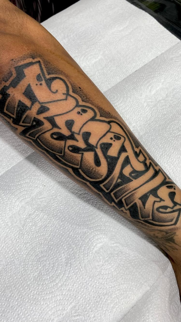 A large black and grey graffiti style lettering tattoo on a person's forearm.