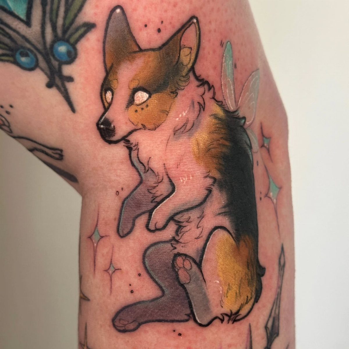 A neo-traditional tattoo of a winged corgi dog on a person's arm.
