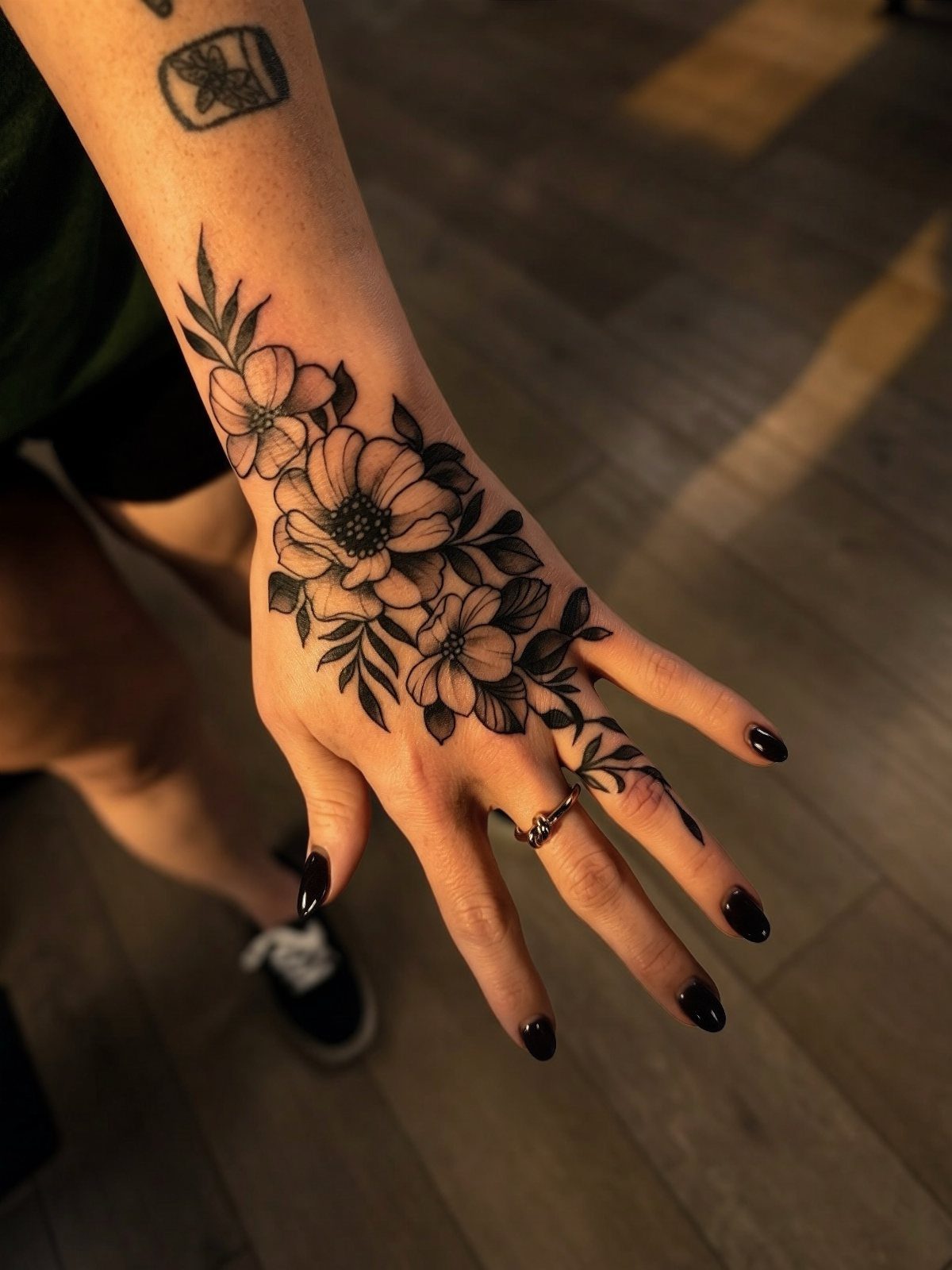 A hand and forearm featuring a detailed black and grey neo-traditional floral tattoo design.