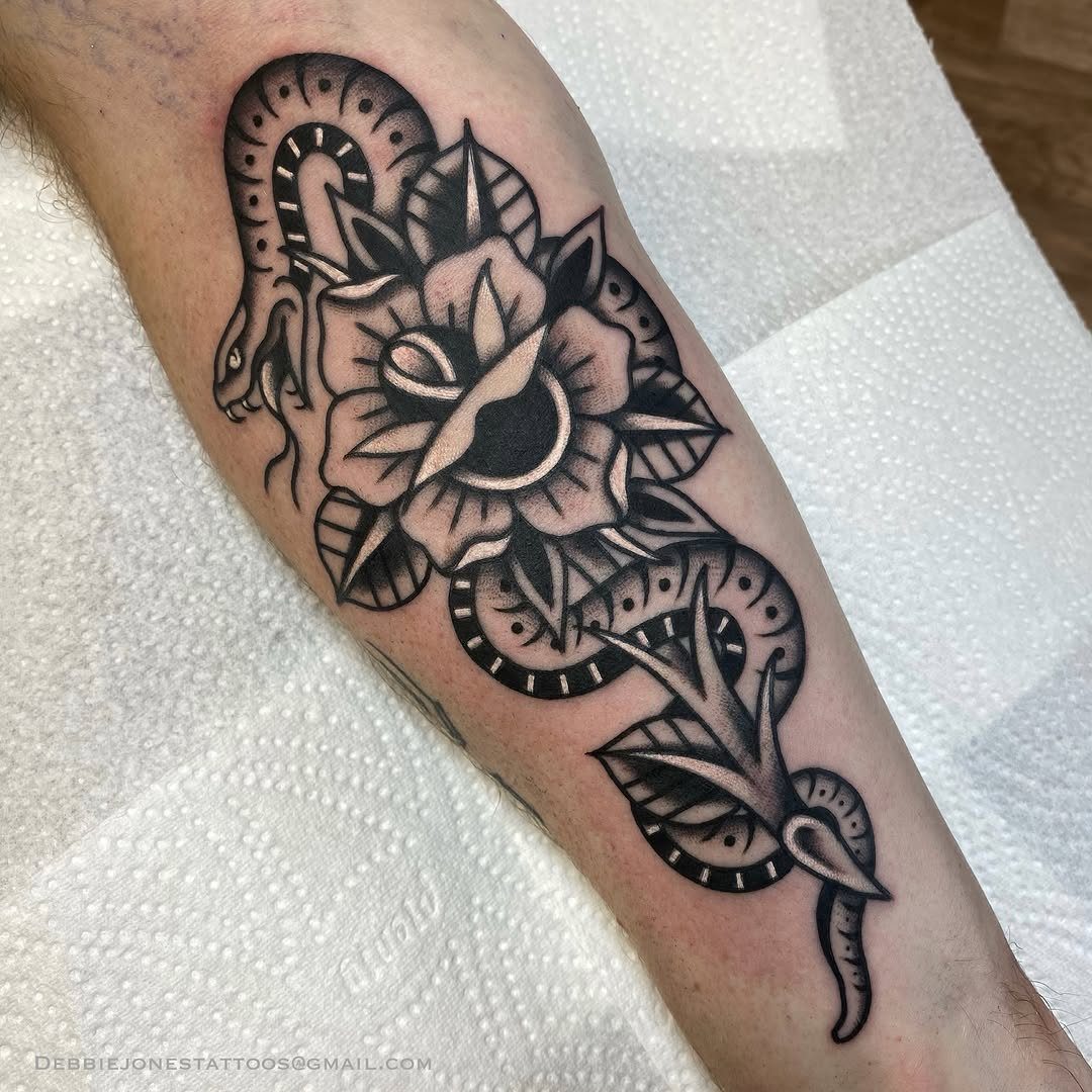 A black and grey neo traditional tattoo of a rose and snake on a forearm.