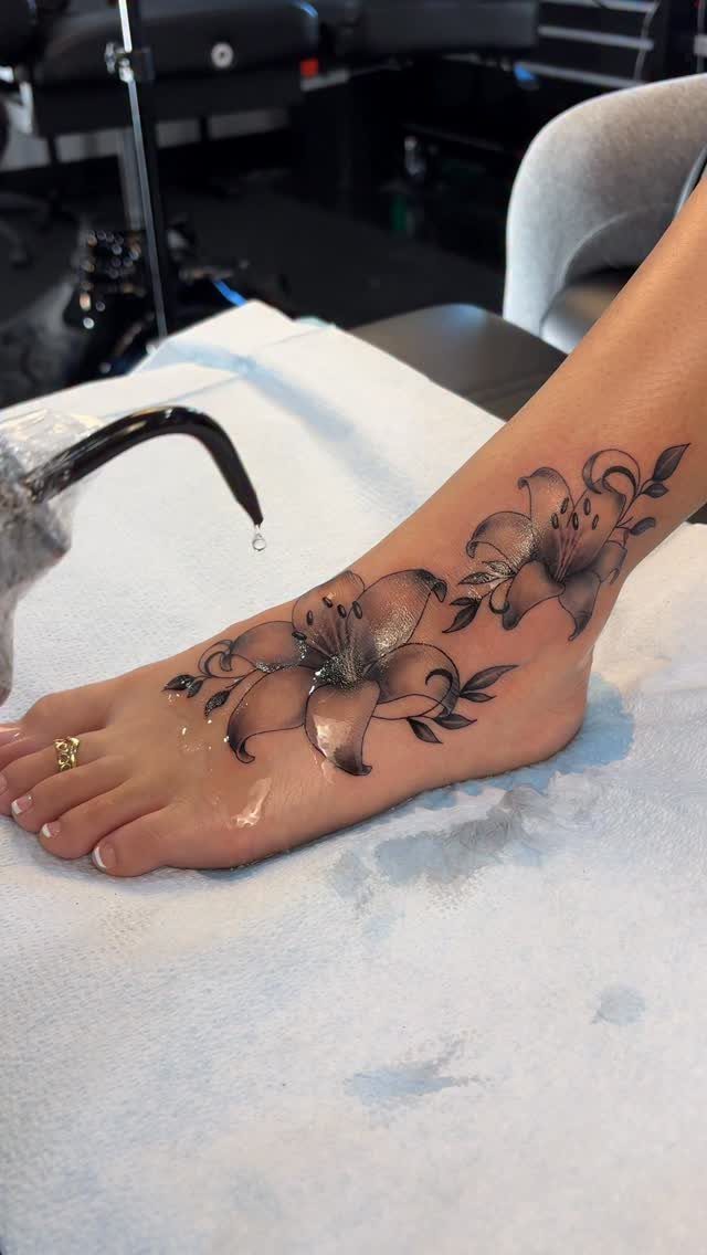 A person's foot decorated with a neo-traditional lily flower tattoo resting on a white towel.