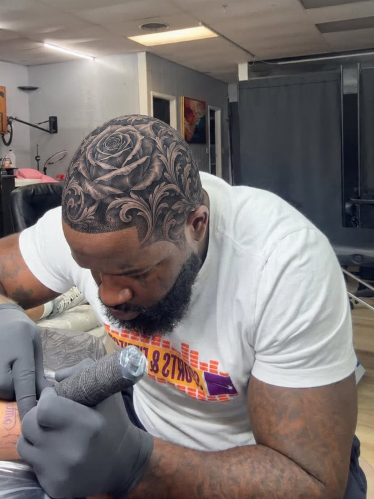 Tattoo Style Victorian: 5 Ideas From Acanthus Scrolls to Portraits 1 A man tattooing an intricate rose and acanthus leaf pattern onto a client's shaved head.